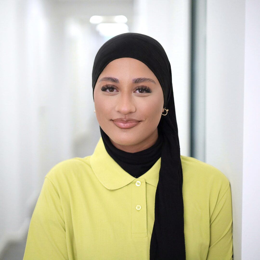 Das Bild zeigt Foto Rabia Akbulut, MFA-Azubine, lächelnd im Portrait vor einem hellen Flur.